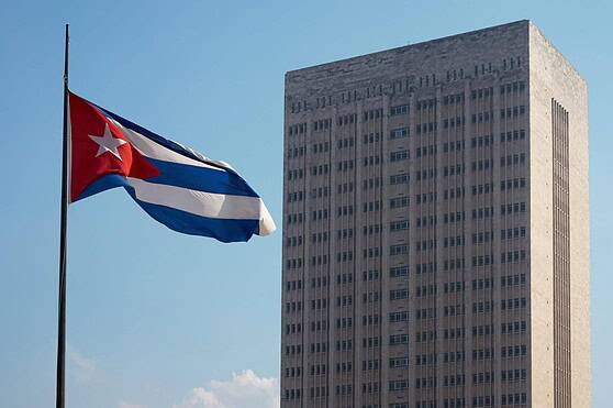 An image featuring the Cuban flag flying next to a high-rise government building, symbolizing international presence and citizenship.