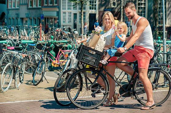 A happy family enjoying a bike ride in a vibrant city, promoting outdoor activity and family bonding amid a backdrop of charming buildings and numerous parked bikes.