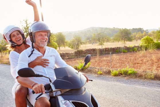 A happy couple riding a scooter through countryside terrain, emphasizing the need for reliable international health insurance coverage when traveling abroad.