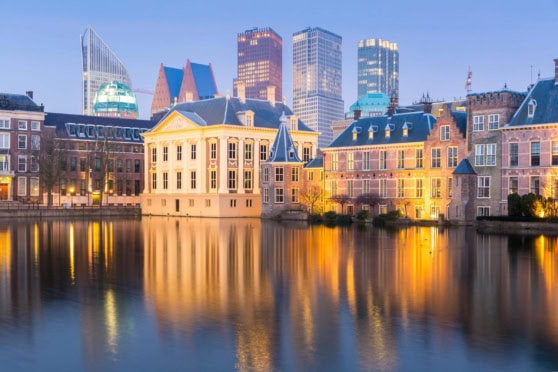 A peaceful view of historic Dutch-style buildings along a calm canal, with a modern city skyline illuminated in the background, capturing the beauty of international urban settings and architectural harmony.