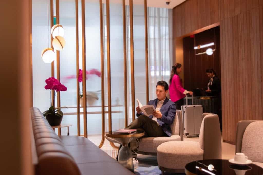 Comfortable airport lounge with traveler waiting and reading, modern decor, luggage in background.