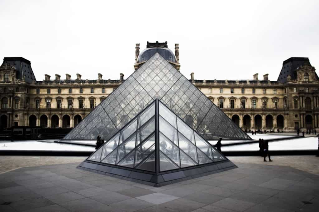 A glass pyramid at the Louvre Museum in Paris, France, reflecting modern architecture against historic buildings, symbolizing cultural heritage and artistic innovation.