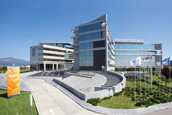 Image of a contemporary healthcare facility with multiple glass-fronted wings, corporate signage, and national flags, representing international health insurance and global medical coverage.