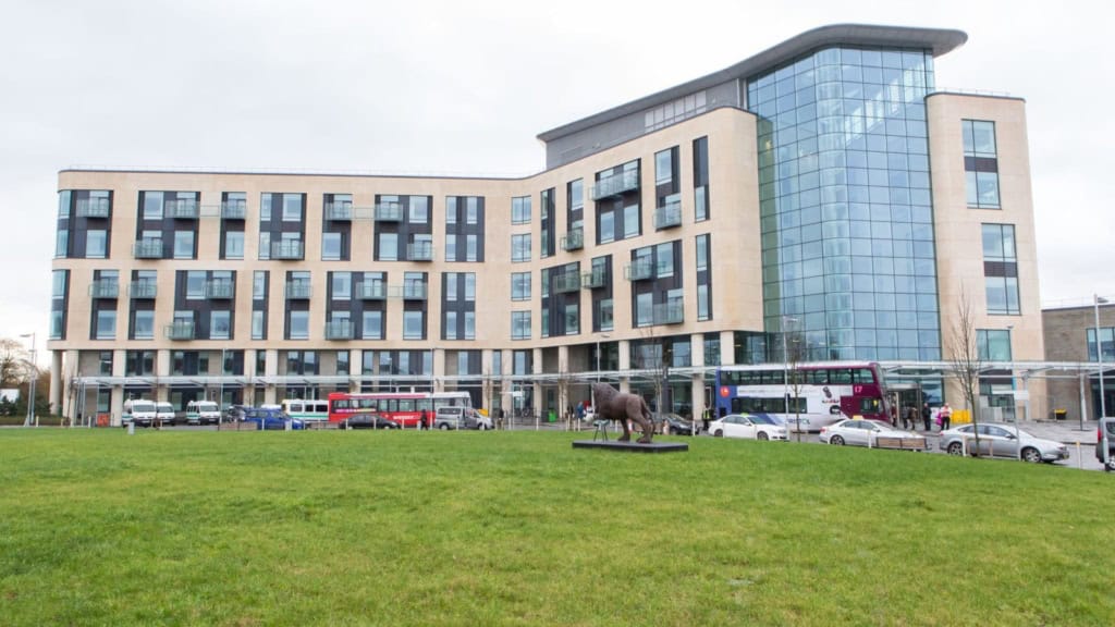 A contemporary office building featuring a glass exterior with multiple floors, set against a cloudy sky, with a lush green lawn and city buses in front, symbolizing global insurance solutions.