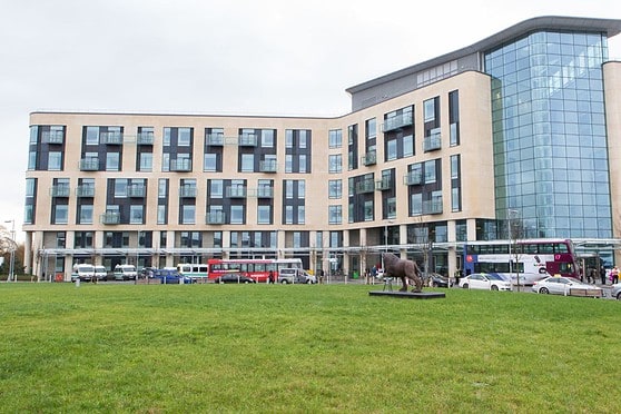 A contemporary office building featuring a glass exterior with multiple floors, set against a cloudy sky, with a lush green lawn and city buses in front, symbolizing global insurance solutions.