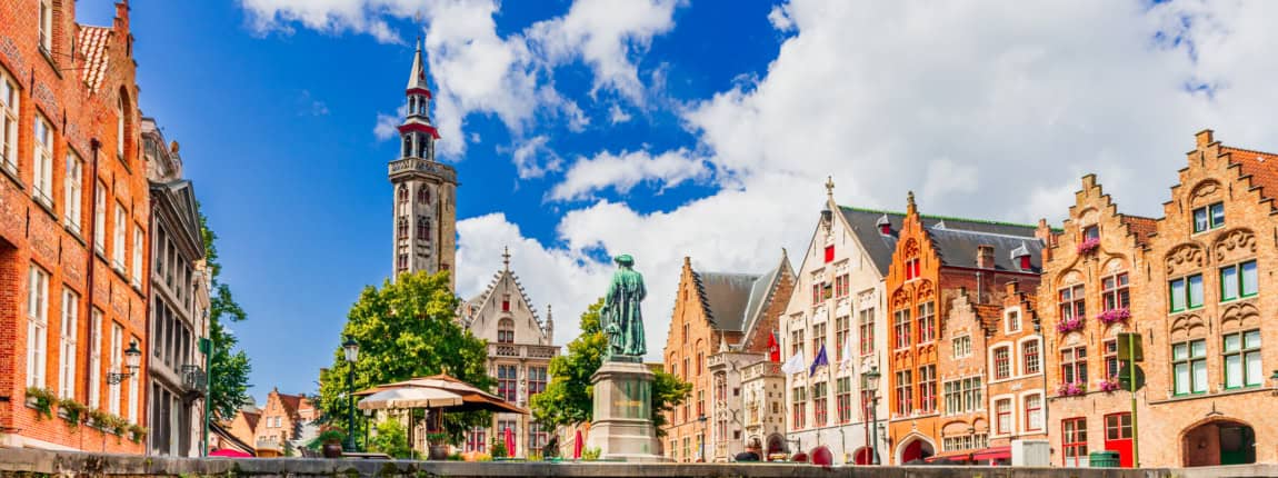 Colorful historic buildings and a church steeple along a canal in Bruges, Belgium, showcasing picturesque architecture, vibrant facades, and scenic waterways, ideal for travel and tourism.
