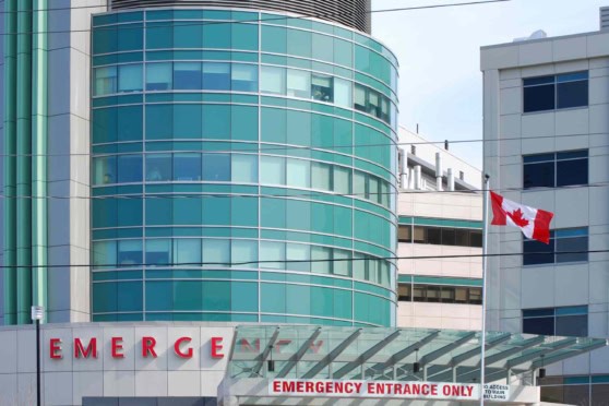 A sleek, contemporary hospital emergency entrance with glass architecture and a Canadian flag, representing global health insurance options for international citizens.
