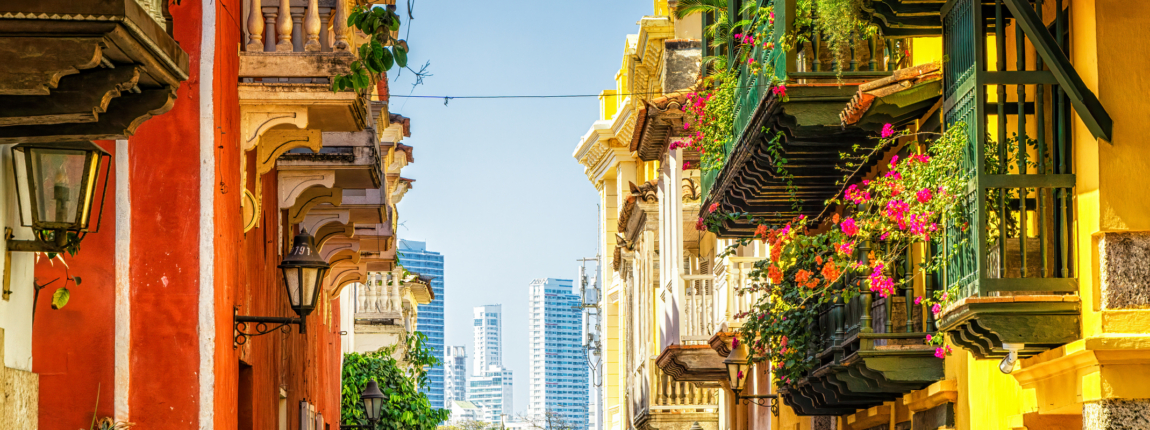 Colorful colonial-style buildings with vibrant facades and lush balconies, showcasing traditional architecture and lively street life, with modern skyscrapers in the background.
