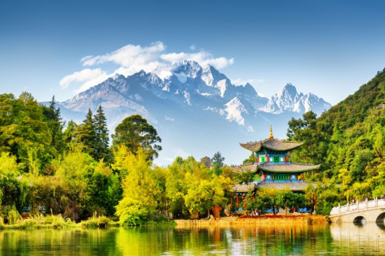 An Asian-style pavilion by a peaceful lake surrounded by vibrant greenery with snow-capped mountains in the background, perfect for travelers seeking international destinations.