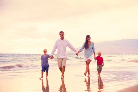 Family of four holding hands and walking along the beach at sunset, emphasizing the importance of international health insurance coverage for travelers abroad.