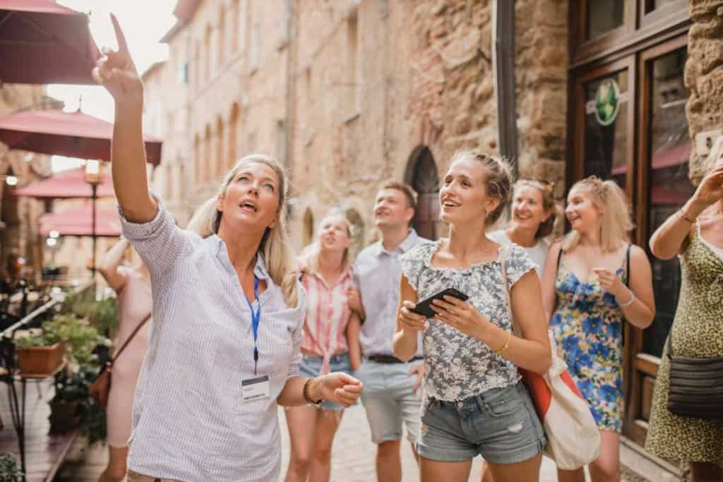 A female tour guide leading a group of tourists, showing them a local building