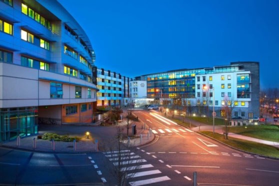 Bright, modern hospital or office complex with multiple floors, glass facades, and surrounding city infrastructure at evening.