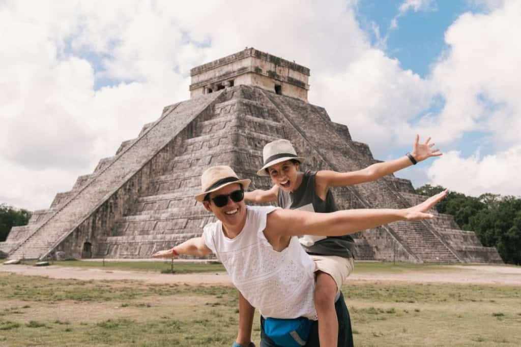 a happy couple posing in front of a pyramid in Mexico, where tourists are advised to buy travel insurance for Mexico