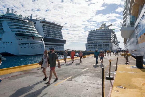 People walking on a cruise port dock near large cruise ships under a partly cloudy sky.