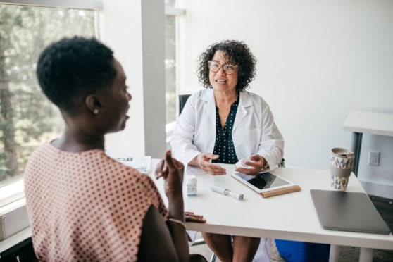 A woman in a pink polka dot dress consults with a doctor in a white coat in a bright, modern clinic for international travel health coverage.