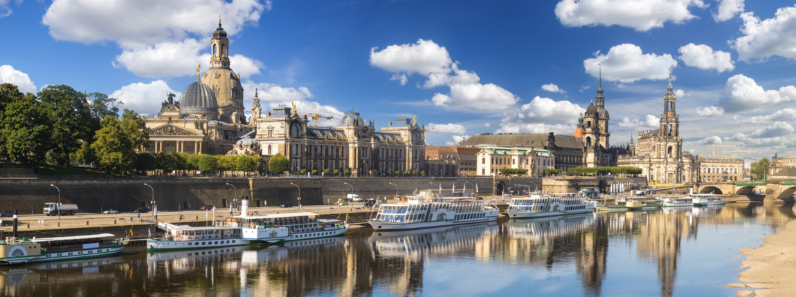 Historic Dresden skyline with Frauenkirche and churches overlooking Elbe River, vibrant cityscape, and blue sky in Germany.