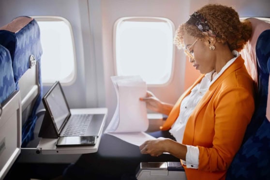 A woman seated on an airplane reviewing documents with a laptop and travel papers, ensuring safety and coverage during her international trip.