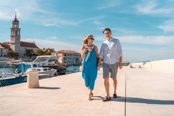 Walking along the harbor, smiling, enjoying sunny day, charming coastal town, vacation, leisure, happiness, senior lifestyle, travel.