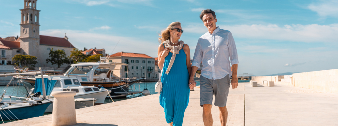 Walking along the harbor, smiling, enjoying sunny day, charming coastal town, vacation, leisure, happiness, senior lifestyle, travel.