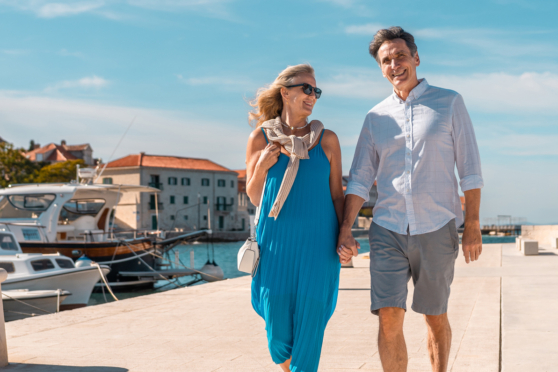 Walking along the harbor, smiling, enjoying sunny day, charming coastal town, vacation, leisure, happiness, senior lifestyle, travel.