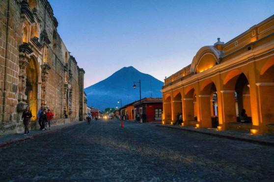Scenic street view of colonial buildings with Mount Atitlán in the background during dusk in Antigua, Guatemala.