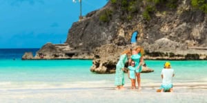 Beautiful family photo at the beach with turquoise water, rocky cliffs, and a bright blue sky, showcasing a perfect travel destination for international travelers.