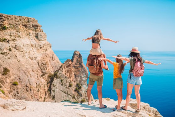 Beautiful outdoor scene of a family of four exploring a seaside cliff, with clear skies, ocean in background, and engaging in sightseeing or nature walk.