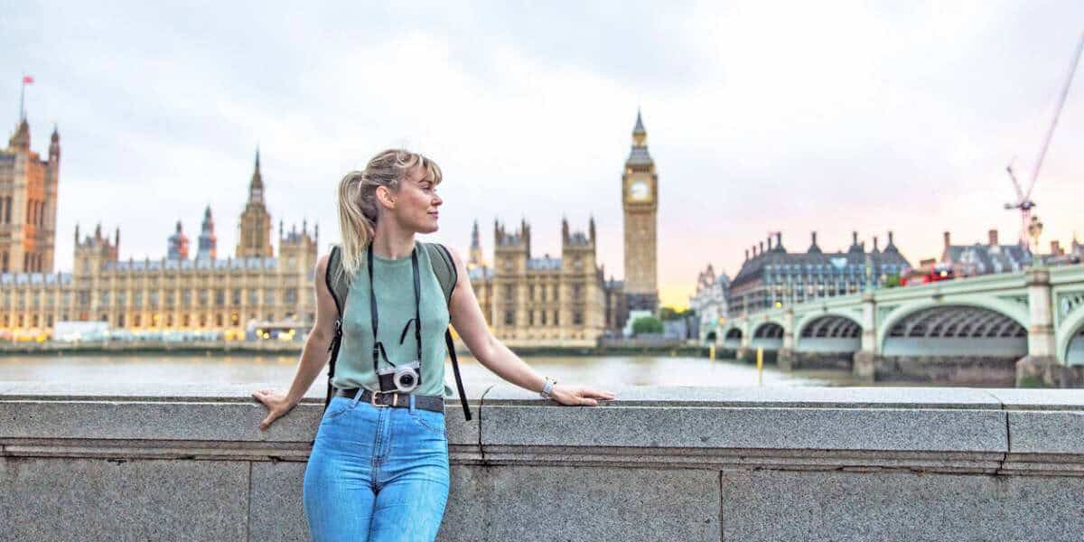 Exploring London, England, a young woman with a camera takes in the iconic cityscape by the River Thames, highlighting international travel and the need for reliable overseas health insurance.