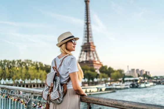 A woman with a backpack enjoys the view of the Eiffel Tower in Paris, symbolizing global travel protection and insurance services for international citizens.