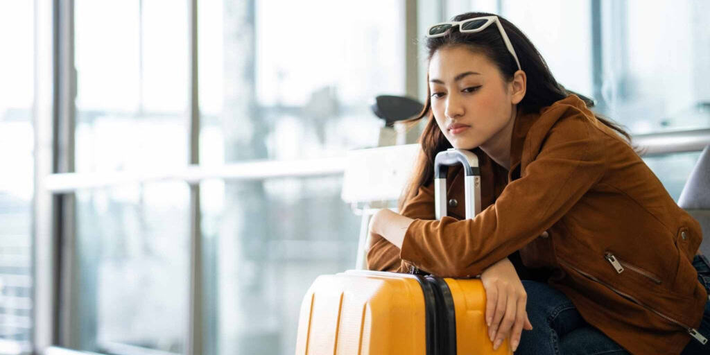 Young woman waiting with luggage at airport, worried about travel issues, representing the need for international travel insurance and coverage solutions for global citizens.