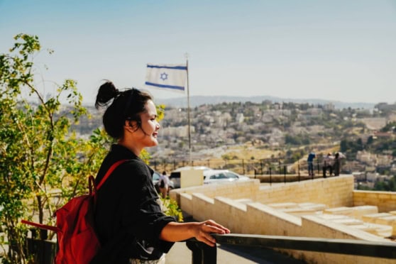 Woman enjoying scenic view of Jerusalem, Israel with national flag, emphasizing international travel and global insurance coverage options.