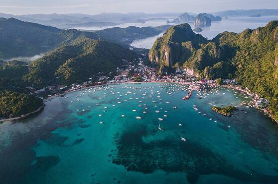 Aerial view of a picturesque coastal village surrounded by lush green mountains, clear blue waters with anchored boats, showcasing travel destinations and international living.