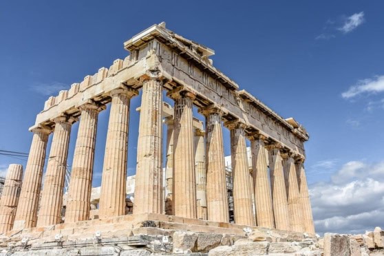 High-resolution image of iconic ancient Greek temple ruins with weathered marble columns under a blue sky, ideal for cultural and historical insurance content.