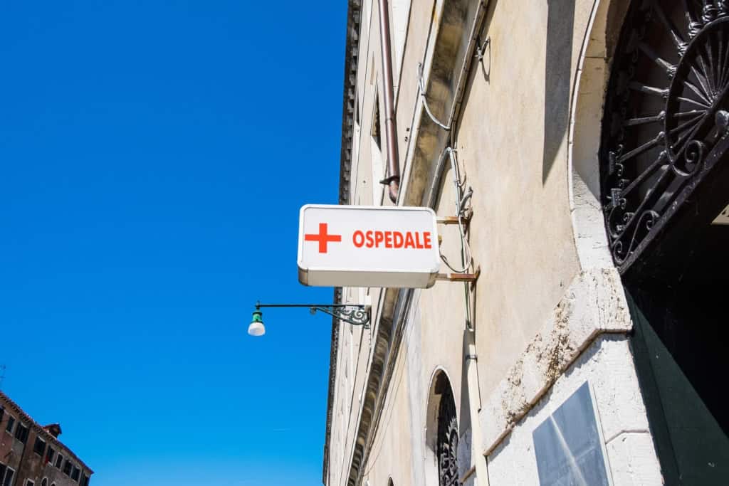 Hospital sign with red cross and “Ospedale” text on building exterior.