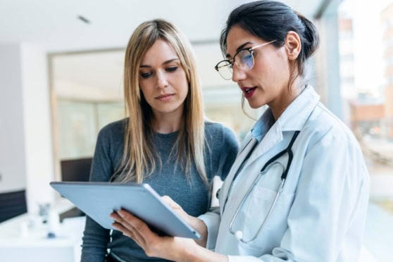 A female doctor consulting with a patient in a modern clinic, reviewing health insurance options on a tablet, representing international health coverage for global citizens and expatriates.