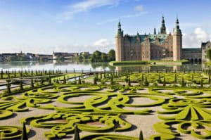 Beautiful Danish castle with lush gardens by the water, featuring intricate topiary and historic architecture, set against a bright blue sky—an iconic scene from ICI 2025.