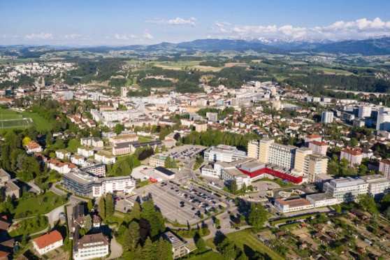 Aerial view of a city with a mix of residential, commercial, and green areas, illustrating urban development and natural landscape in the background.