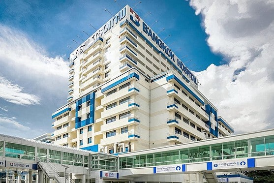 A modern high-rise Bangkok Hospital with clear signage, large windows, and a glass entrance, under a bright sky, representing international healthcare facilities for global citizens.