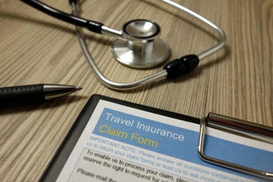 Stethoscope and pen on wood desk, insurance claim form for travel health coverage, highlighting international insurance benefits for travelers.