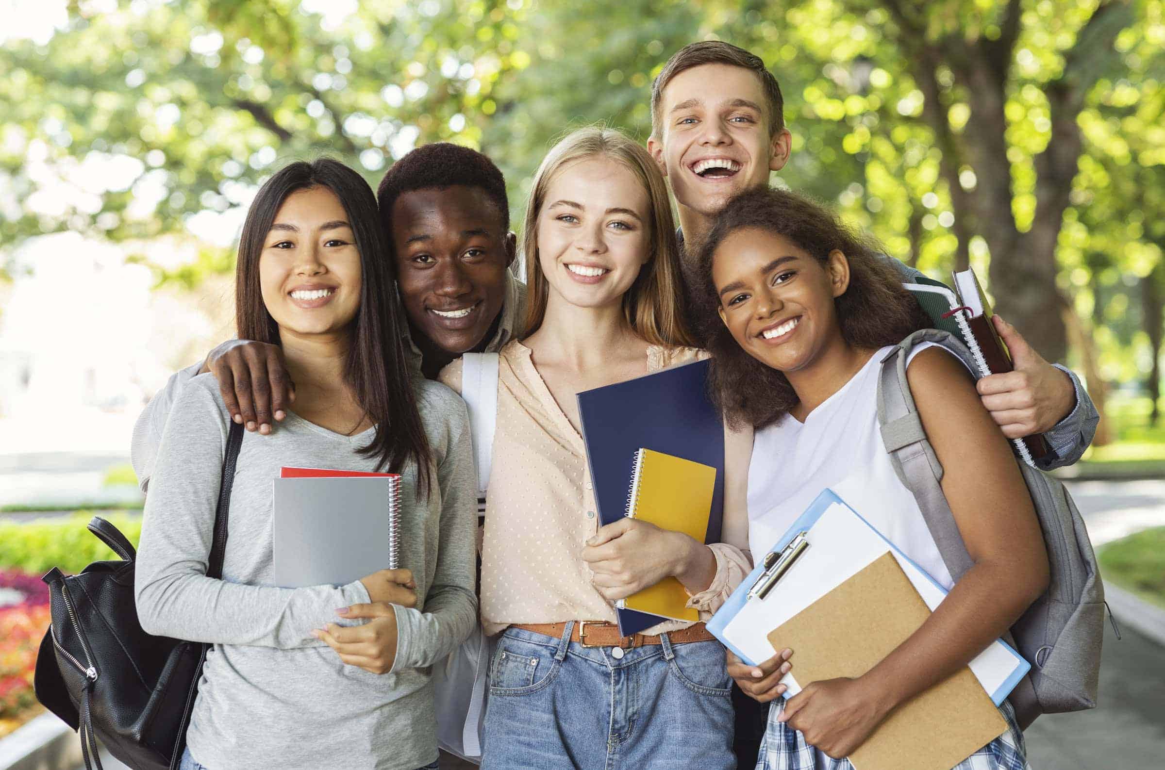 Diverse group of young students outdoors, smiling, holding notebooks and backpacks, representing global health insurance solutions for international citizens.