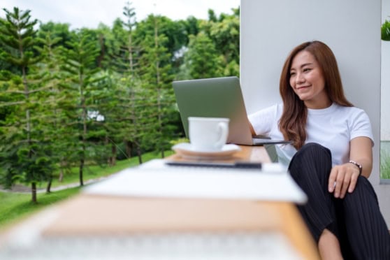 A young woman working remotely with a laptop outdoors, surrounded by lush green trees, showcasing international health insurance coverage for global citizens and expatriates.