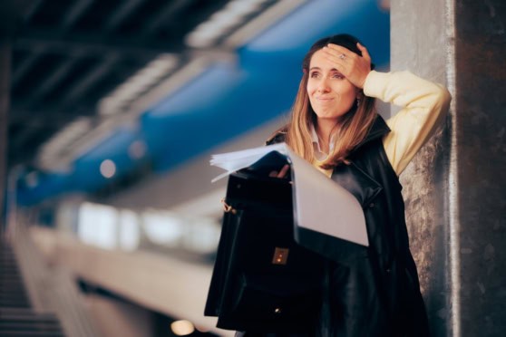 Overwhelmed woman at airport, distressed about travel delays or missed connections, holding papers and leaning against a pillar.