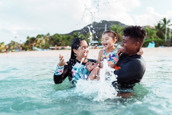Family playing joyfully in the ocean, representing international travel, health, and life insurance for global citizens enjoying beach vacations.