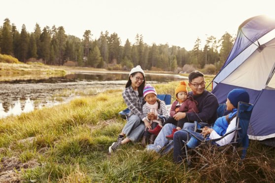 Bright, cheerful family outdoor camping scene by a lake, emphasizing the importance of international health insurance and travel protection for global citizens.