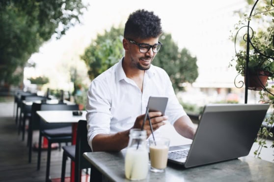 A happy man using a smartphone and laptop outdoors, promoting international health coverage.