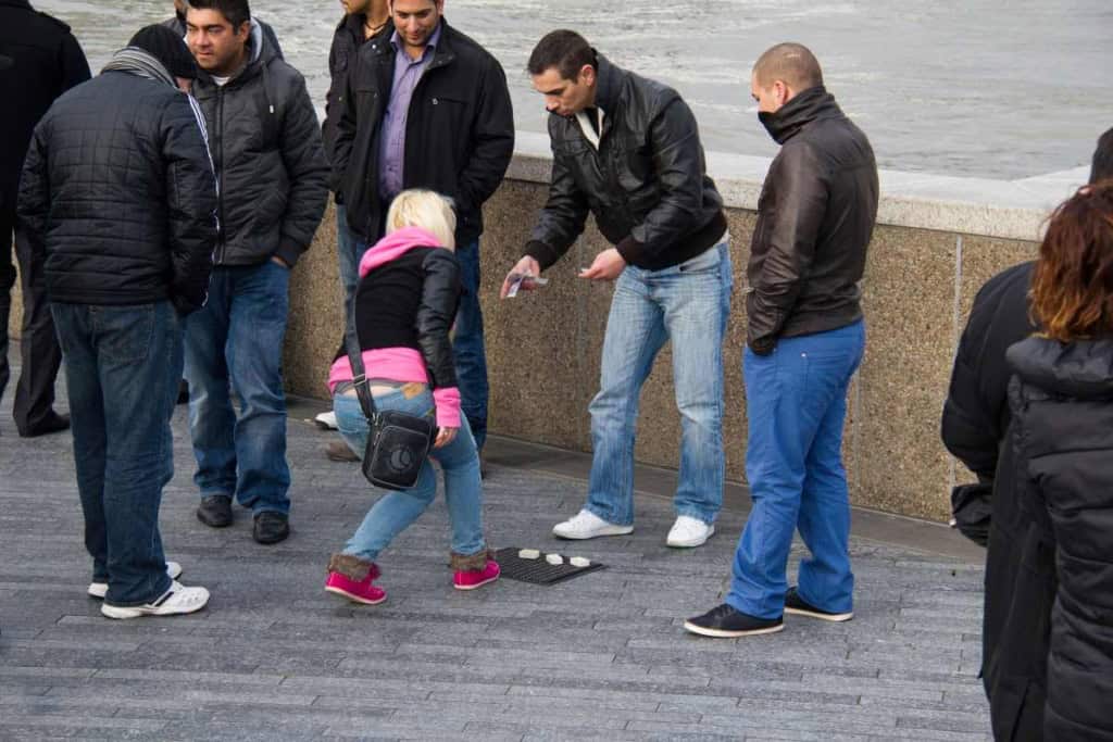 a female tourist falling victim to one of the shell game travel scams in London, UK
