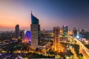A bustling cityscape with tall modern buildings lit up at sunset, highlighting international city life and global business hubs.
