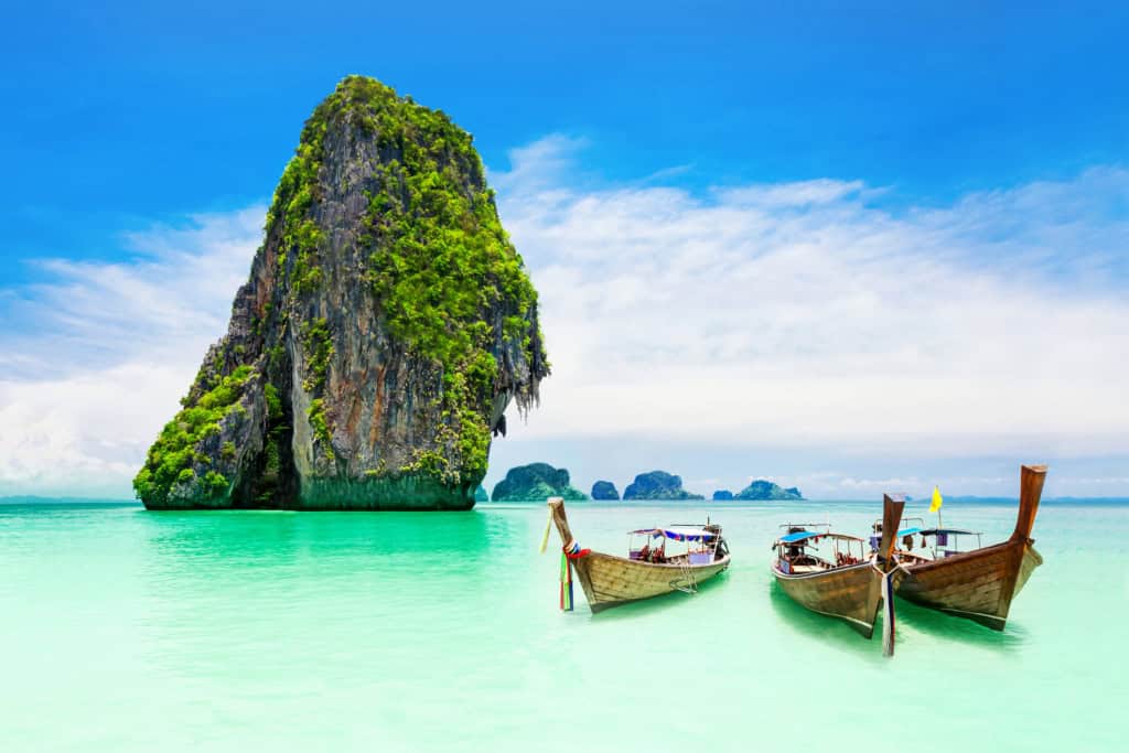 An idyllic tropical island scene featuring limestone cliffs, pristine turquoise waters, and classic wooden longtail boats, ideal for international travelers and expats seeking adventure and relaxation.