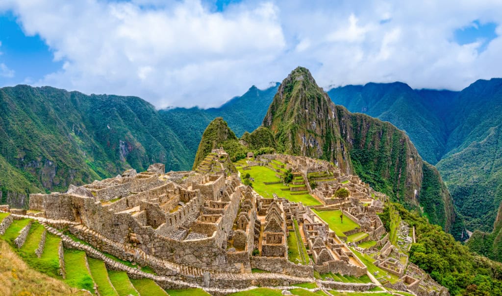 Ancient Incan ruins at Machu Picchu in the Andes mountains, showcasing stone terraces and architecture amidst lush green scenery with a dramatic mountain backdrop.