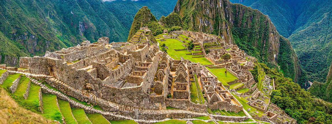 Ancient Incan ruins at Machu Picchu in the Andes mountains, showcasing stone terraces and architecture amidst lush green scenery with a dramatic mountain backdrop.